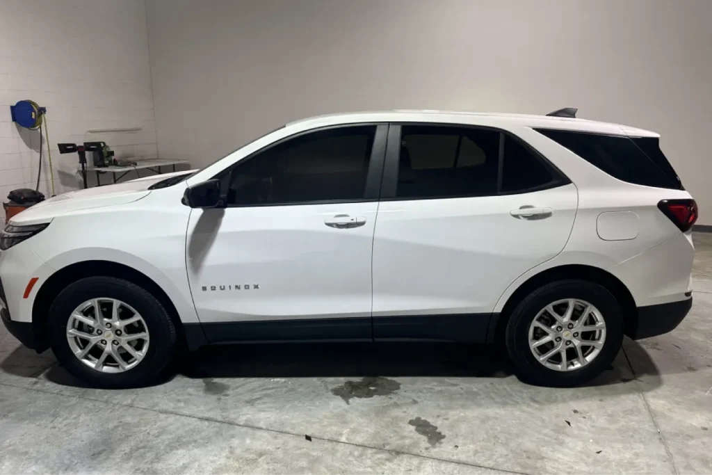 Rear side view of a white Chevrolet Equinox with tinted windows, parked indoors.