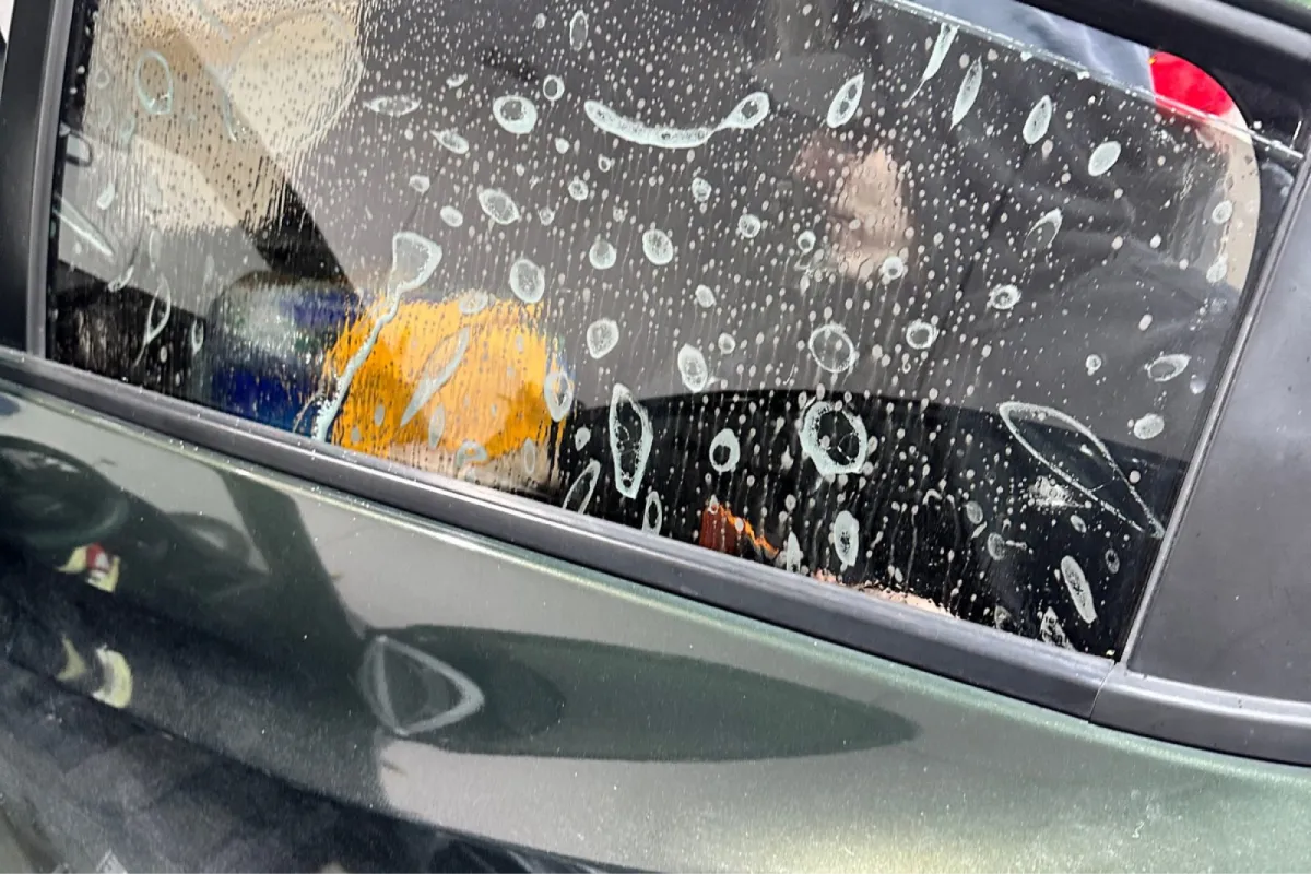 Car window covered in soapy solution during tint installation.